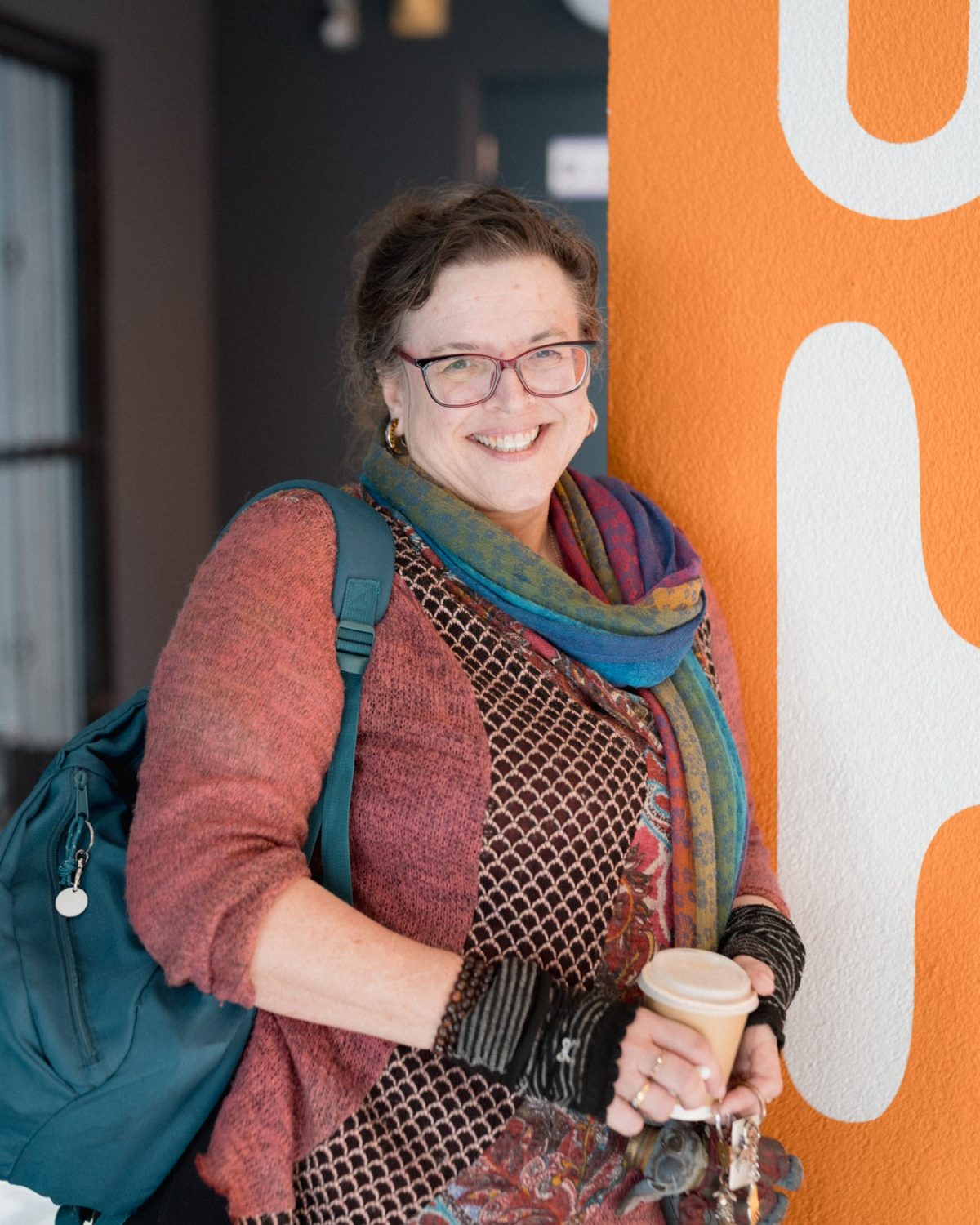 A woman wearing glasses and a colorful scarf, standing in front of an Urban HQ wall