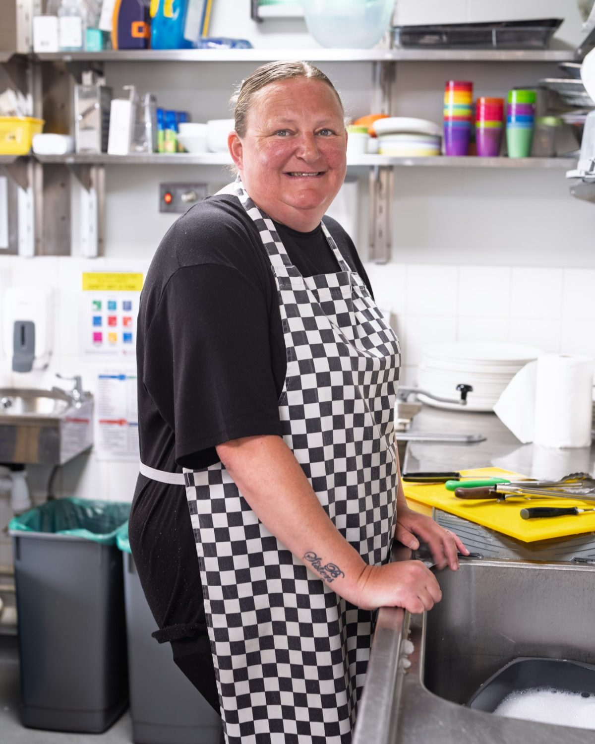 A woman preparing food in a bright kitchen with a checkered apron on and cutting utensils nearby