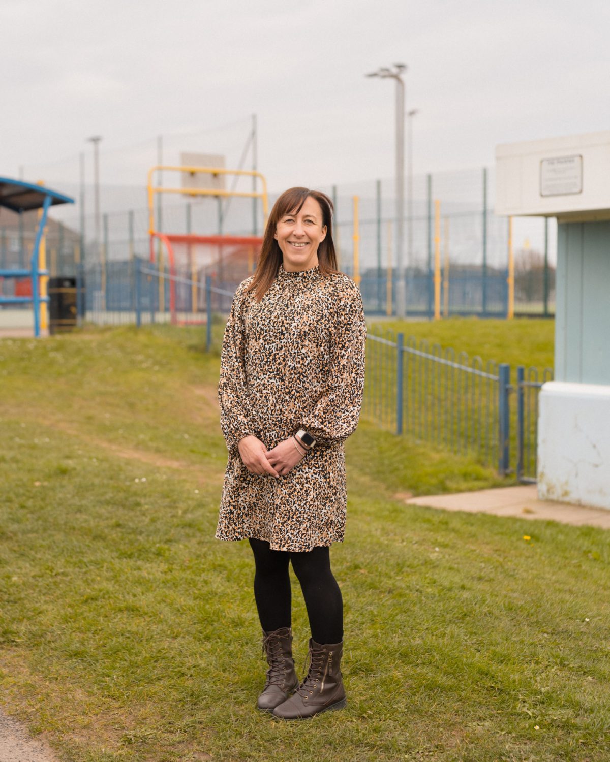 A woman with an animal print dress on stood in a field in front of a basketball court