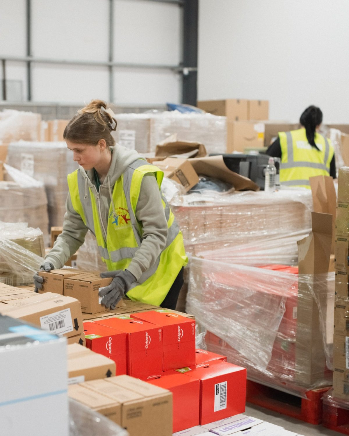 Two women with high-vis vests on packing boxes in a warehouse