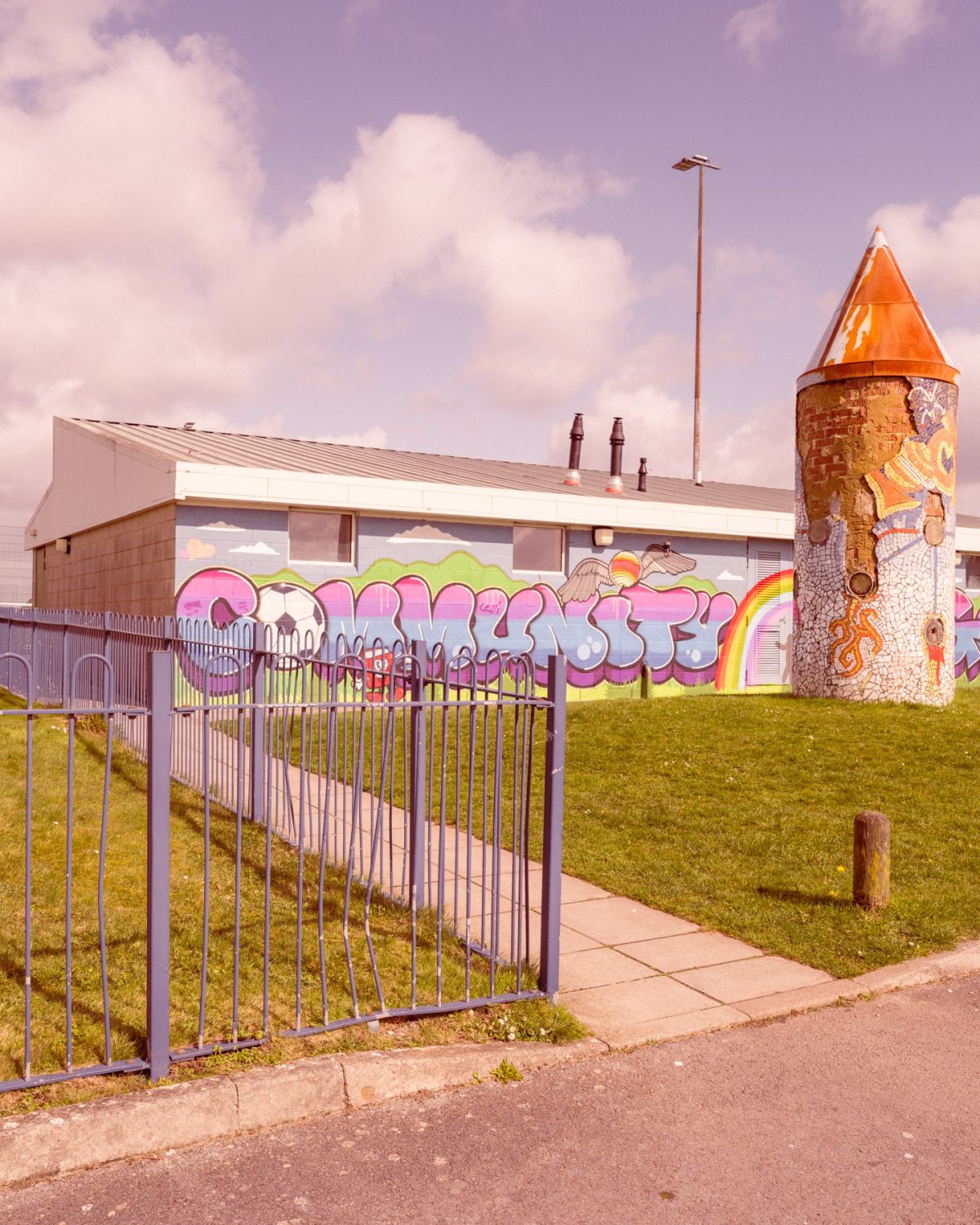 A building surrounded by grass and a cloudy sky with colourful graffiti writing that says 'community'