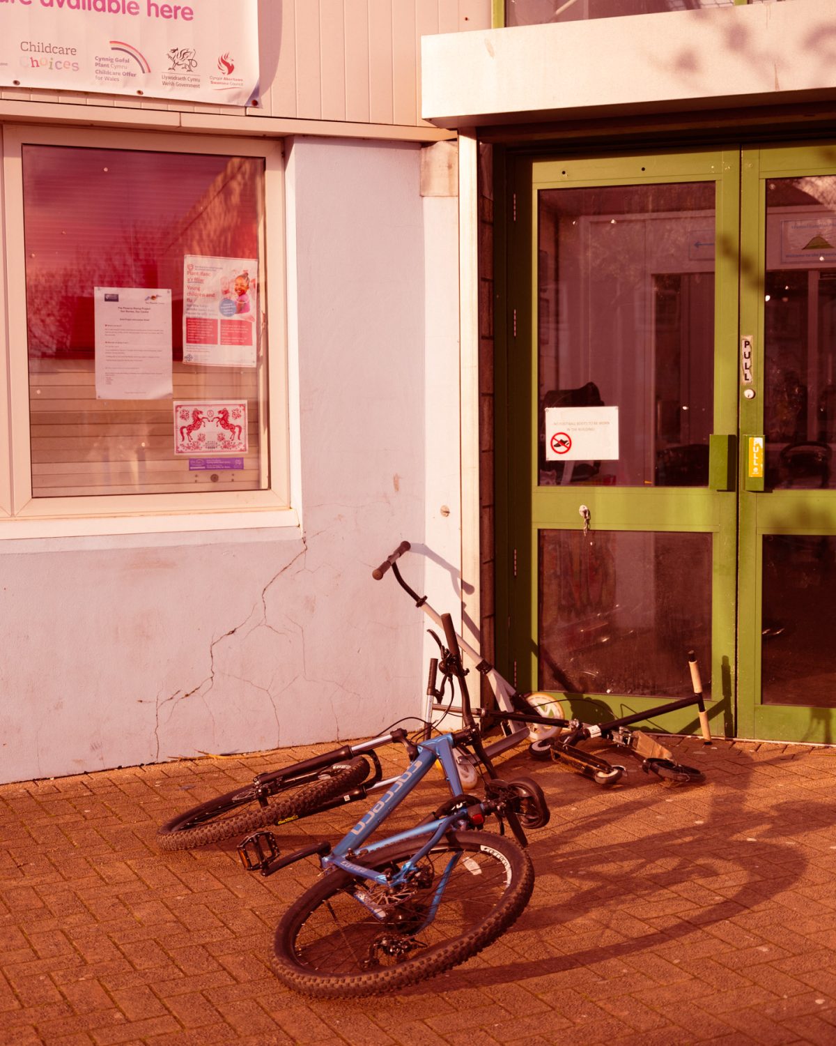 A bicycle and a scooter leaning on the floor outside of a building