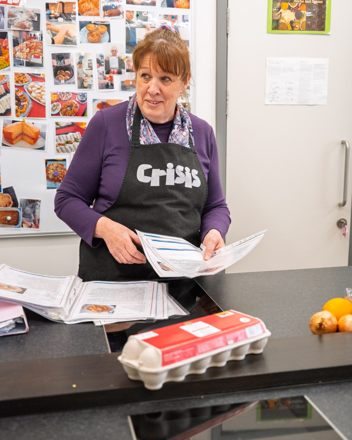 A woman with a crisis-branded apron following a recipe in a kitchen