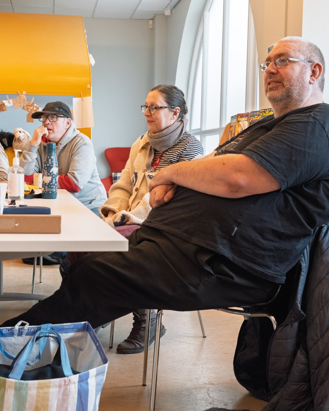 A group of people in a bright room sat around a table listening