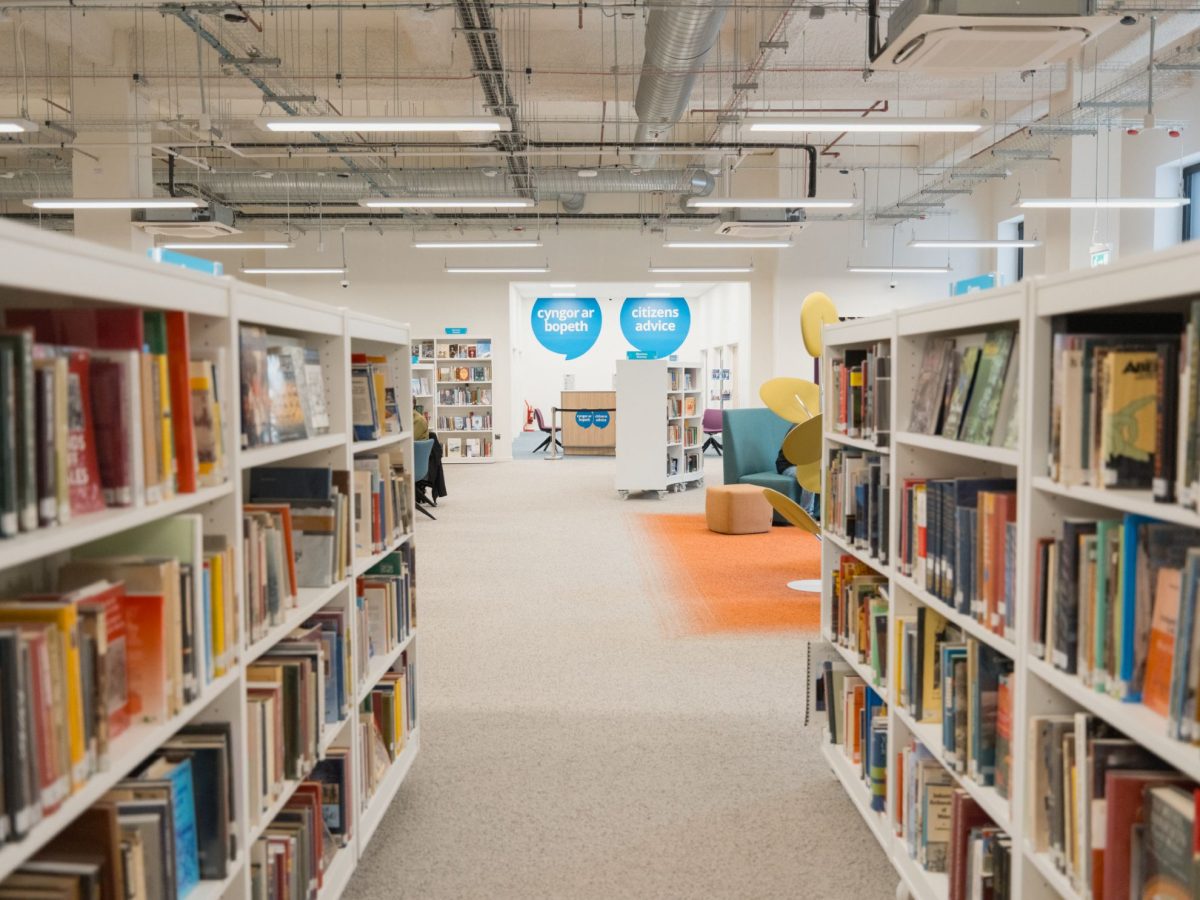 A multi-use hub with bookshelves in the foreground and a help desk in he background