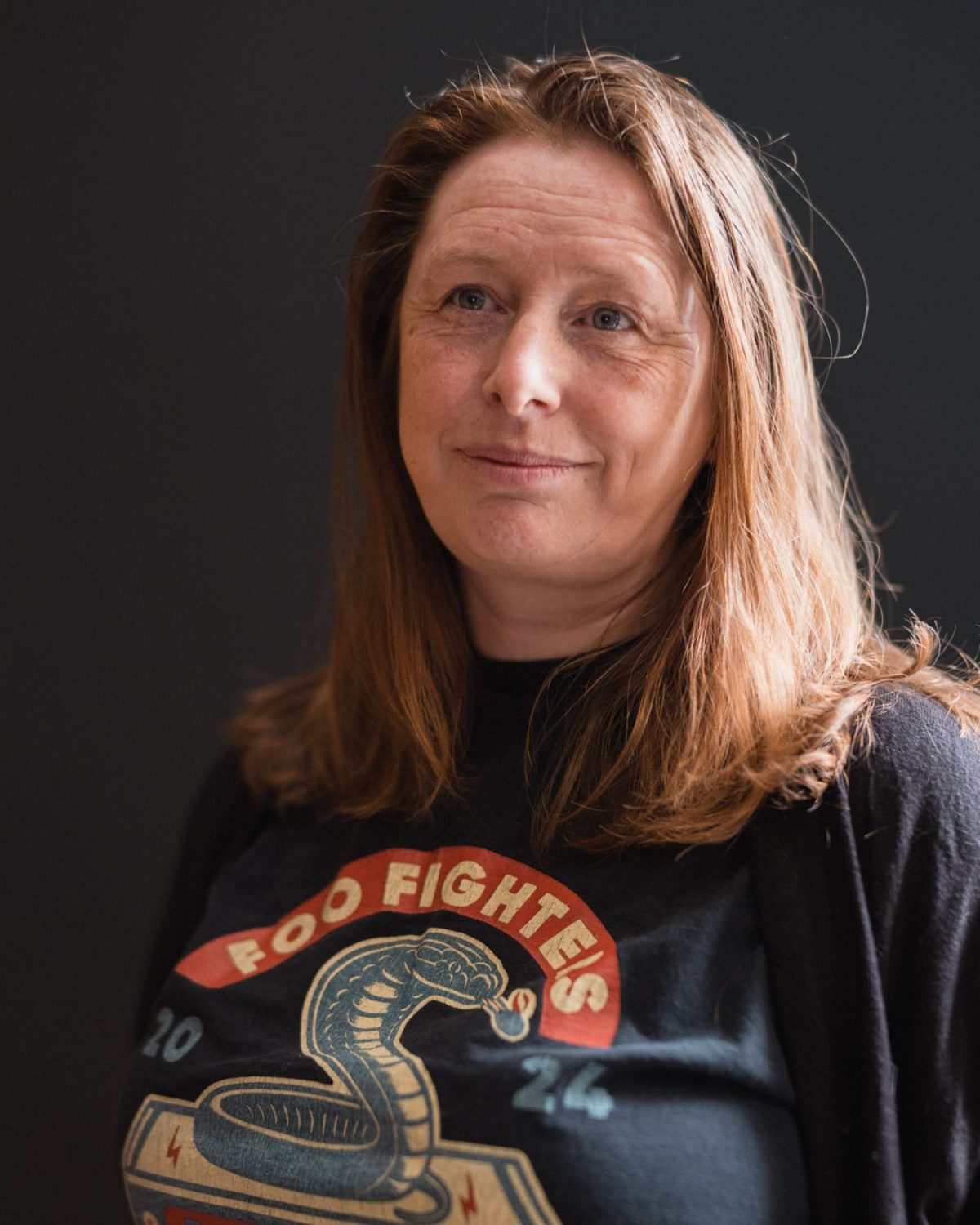A woman with brown hair and a graphic-style t-shirt posing for the camera with a dark background